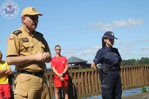 Zdjęcie kolorowe. Strażak i policjantka stoją przed liczną grupą dzieci