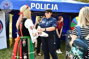 Zdjęcie kolorowe. Kobieta w stroku ludowym częstuje policjantkę chlebem