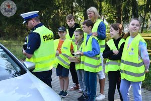 Zdjęcie kolorowe. Policjant w towarzystwie dzieci rozmawia z kierowcą