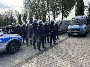 Zdjęcie kolorowe. Policjanci z tarczami i w białych kaskach stoją w szeregu