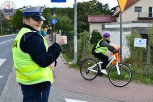 Zdjęcie kolorowe. Policjantka obserwuje przejazd ścieżką rowerową rowerzystów na trasie