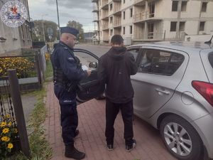 Zdjęcie kolorowe. Policjant stoi obok mężczyzny przy samochodzie