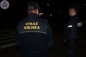 Zdjęcie kolorowe. policjant i strażnik miejski odwróceni plecami