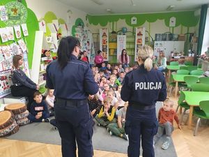 Zdjęcie kolorowe. Policjantki zwrócone plecami rozmawiają z dziećmi