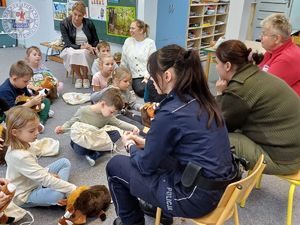 Zdjęcie kolorowe. Na małych krzesełkach przed siedzącymi na dywanie dziećmi siedzi policjantka funkcjonariuszka służby leśnej i promotor zdrowia z sanepidu