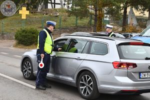 Zdjęcie kolorowe. Policjant kontroluje kierującego w srebrnym samochodzie