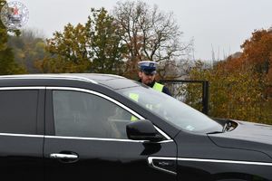 Zdjęcie kolorowe. Policjant kontroluje kierującego w czarnym samochodzie