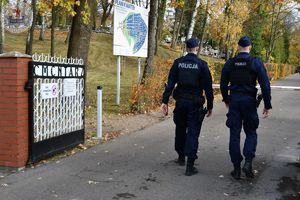 Zdjęcie kolorowe. Policjanci wchodzą na teren cmentarza