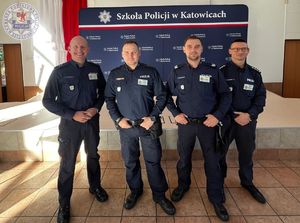 Zdjęcie kolorowe. Policjanci pozują na ściance Szkoły Policji w Katowicach