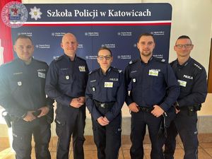 Zdjęcie kolorowe. Policjanci pozują na ściance Szkoły Policji w Katowicach