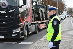 Zdjęcie kolorowe. Policjant ruchu drogowego kieruje ruchem na przejściu dla pieszych