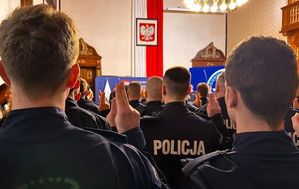 Zdjęcie kolorowe. Policjanci odwróceni tyłem mają podniesione ręce złożone do ślubowania