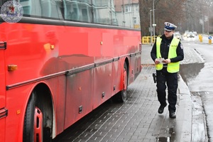 Zdjęcie kolorowe. Policjant przechodzi obok czerwonego autobusu