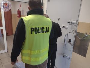 Zdjęcie kolorowe. Policjant w kamizelce odblaskowej stoi odwrócony plecami