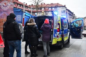 Zdjęcie kolorowe. Osoby odwiedzające stanowisko policji oglądają radiowóz robią sobie pamiątkowe zdjęcie