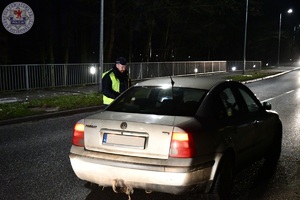 Zdjęcie kolorowe. Zdjęcie zrobione w nocy. Policjant kontroluje kierującego na zawartość alkoholu w wydychanym powietrzu