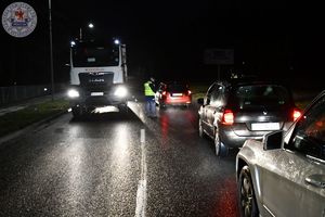 Zdjęcie kolorowe. Zdjęcie zrobione w nocy. Policjant kontroluje kierującego na zawartość alkoholu w wydychanym powietrzu