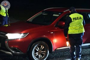 Zdjęcie kolorowe. Zdjęcie zrobione w nocy. Policjant kontroluje kierującego na zawartość alkoholu w wydychanym powietrzu