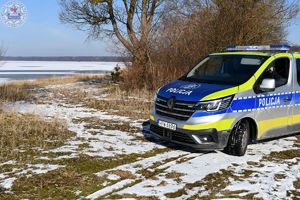 Zdjęcie kolorowe. Policjanci kontrolują linię brzegową przy zamarzniętym jeziorze