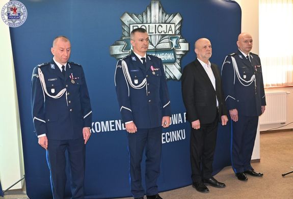 Zdjęcie kolorowe. Na niebieskiej ściance z policyjna gwizdką od lewej stoi Komendant Powiatowy, następnie Komendant Wojewódzki, Starosta i I Zastępca Komendanta Powiatowego