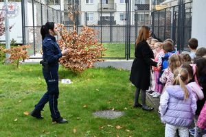 Zdjęcie kolorowe. Policjantka rozmawia z dziećmi na tle wybiegu dla psów