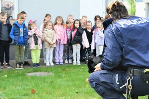 Zdjęcie kolorowe. Policjant kuca w tle dzieci