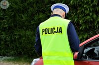 Zdjęcie kolorowe. Policjant odwrócony plecami w kamizelce odblaskowej z napisem policja