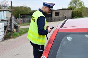 Zdjęcie kolorowe. Policjant rozmawia z kierującym siedzącym za kierownicą auta