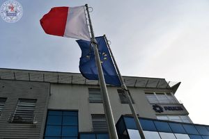 Zdjęcie kolorowe. Flaga biało czerwona Rzeczypospolitej Polskiej i Unii Europejskiej przed budynkiem szczecineckiej policji