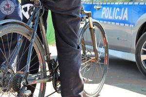 Zdjęcie kolorowe. Rowerzysta zbliżenie kół roweru na tle radiowozu
