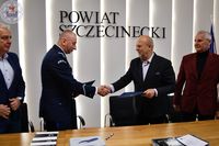 Zdjęcie kolorowe. Na ścianie napis powiat szczecinecki, na jej tle komendant podaje rękę staroście