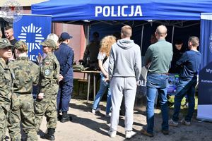 Zdjęcie kolorowe. Niebieski namiot z napisem policja i zgromadzeni wokół niego uczestnicy dni otwartych