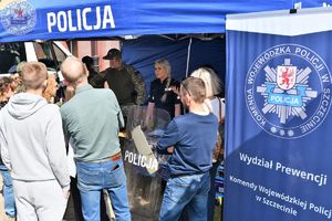 Zdjęcie kolorowe. Niebieski namiot z napisem policja i zgromadzeni wokół niego uczestnicy dni otwartych