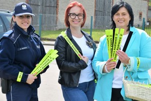 Zdjęcie kolorowe. Dwie kobiety w towarzystwie policjantki pozują do zdjęcia z opaskami odblaskowymi