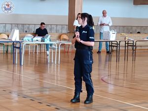 Zdjęcie kolorowe. Policjantka w sali gimnastycznej przemawia do uczniów