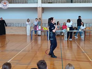 Zdjęcie kolorowe. Policjantka w sali gimnastycznej przemawia do uczniów