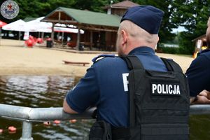 Zdjęcie kolorowe. Policjanci obserwują plaże  jeziora Trzesiecko