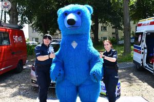 Zdjęcie kolorowe. Policjantki stoją u boku niebieskiego misia