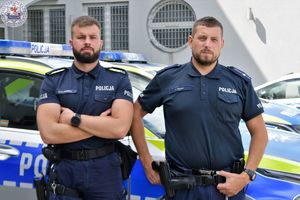 Zdjęcie kolorowe. Policjanci na tle radiowozu