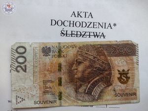 Zdjęcie kolorowe. Na aktach z napisem akta dochodzenia skreślone linią słowo śledztwa, poniżej banknot 200 zł