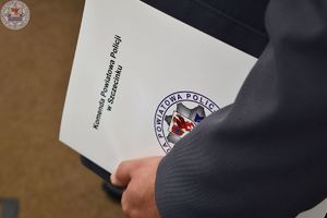 Zdjęcie kolorowe. Zbliżenie trzymanej w rękach białej teczki wzdłuż ciała z napisem Komenda Powiatowa Policji w Szczecinku