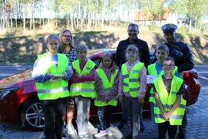 Zdjęcie kolorowe. Policjant w towarzystwie uczniów ubranych w kamizelki odblaskowe