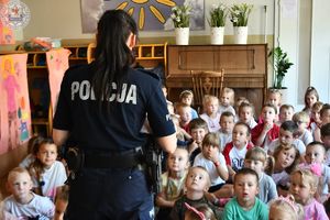 Zdjęcie kolorowe. Policjantka zwrócona do dzieci. Na plecach napis policja