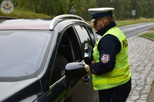 Zdjęcie kolorowe. Policjant rozmawia z kierującym zatrzymanym do kontroli