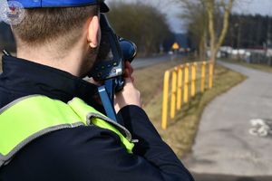 Zdjęcie kolorowe. Policjant dokonuje pomiaru prędkości na drodze