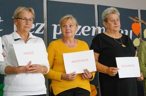 Zdjęcie kolorowe. Trzy kobiety trzymają białe kartki na nich zapisane słowa np akceptacja