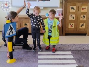 Zdjęcie kolorowe. Policjantka przeprowadza przedszkolaków przez matę na której jest namalowane przejście dla pieszych