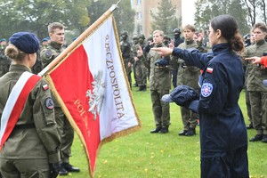 Zdjęcie kolorowe. Uczennica klasy policyjnej z wyciągniętą dłonią ślubuje na sztandar