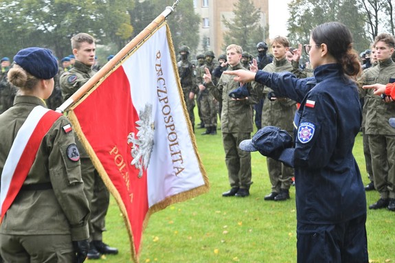 Zdjęcie kolorowe. Uczennica klasy policyjnej z wyciągniętą dłonią ślubuje na sztandar