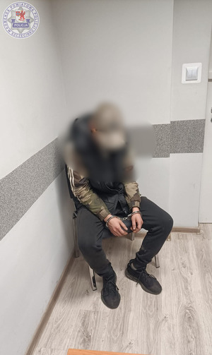 Zdjęcie kolorowe. Policjant doprowadza zatrzymanego mężczyznę